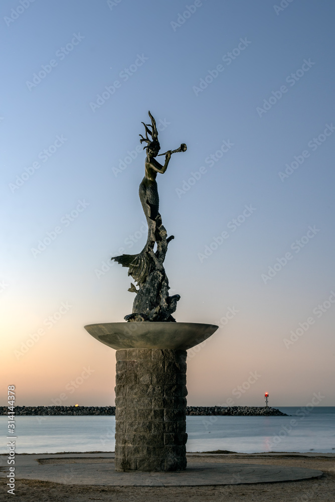 Φωτογραφία Ventura Harbor statue glows in the morning sunrise as the fog lights shine at end of ocean jetty