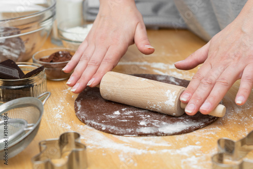 Female hands rolling chocolate dough with rolling-pin. Cooking homemade cookies or pastry, dessert.