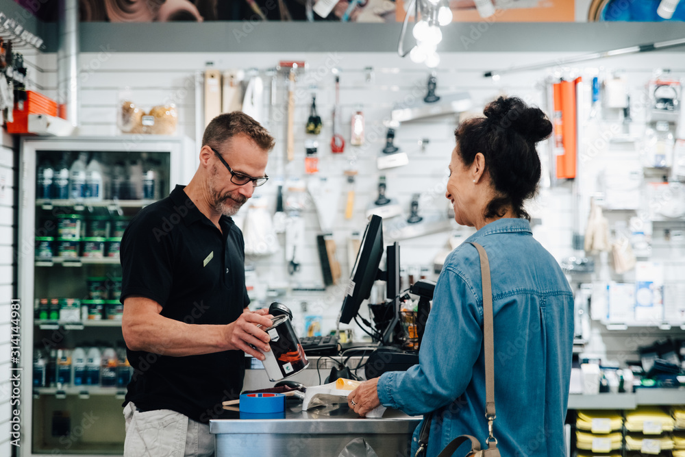 Male cashier talking with Customer at checkout counter in hardware store Male cashier talking with Customer at checkout counter in hardware store