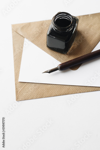 set of vintage dip pen, inkpot and blank paper sheet with envelope on white wooden table