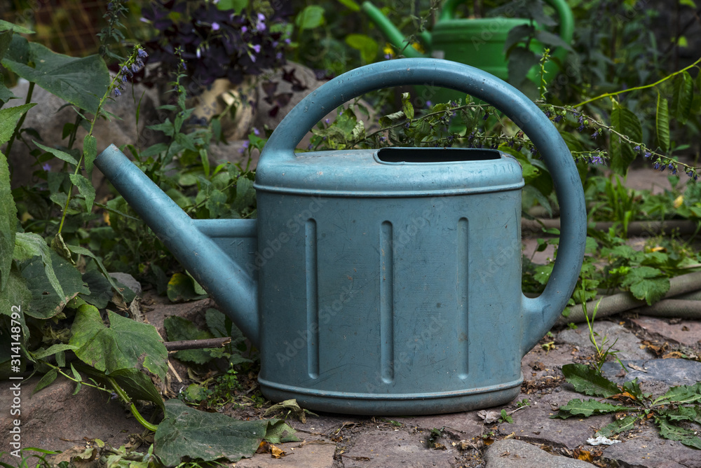 Old scratched plastic watering can stands on the stones in the garden Old scratched plastic watering can stands on the stones in the garden