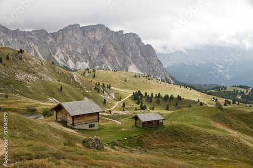 Hütten Wanderung auf der Almwiese der Alm im Herbst in den Dolomiten mit schöner Bergkulisse der Seceda im Grödner Tal in Südtirol Italien in Europa. Berghütten und Nebel und Wolken.