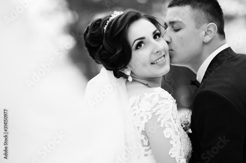 Sensual Black and white foto of bride and groom. Stylish couple of happy newlyweds posing and kisses in the park on their wedding day. Together. The concept of youth, love, fashion and and lifestyle.
