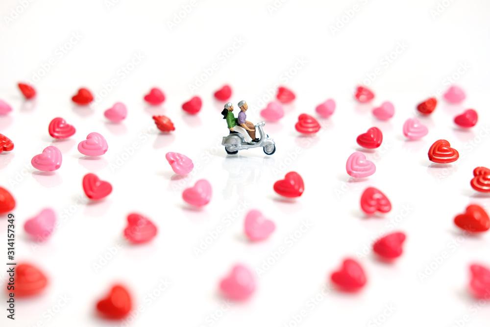 Miniature / toys photography for valentines day - young couple riding scooter with I love you beads on shiny white background