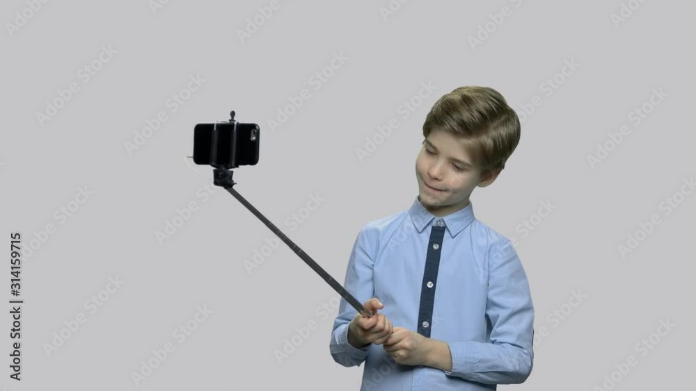 Little boy fooling around while making photos. Cute funny child grimacing. Kid using selfie stick against gray background. Little boy fooling around while making photos. Cute funny child grimacing. Kid using selfie stick against gray background.