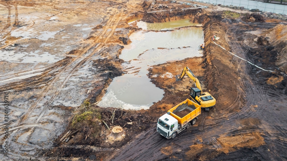 Aerial photo of excavator pours sand into the truck. On the construction site top view. Shooting from the drone