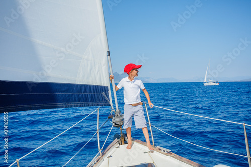 Little boy on board of sailing yacht on summer cruise. Travel adventure, yachting with child on family vacation. photo