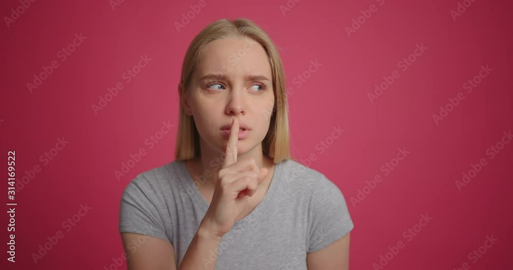 Suspicious girl putting finger to lips making silence gesture at pink wall Suspicious girl putting finger to lips making silence gesture at pink wall