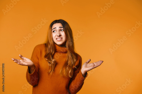 Young girl has apologized look and spreads her hands on the orange banner background
