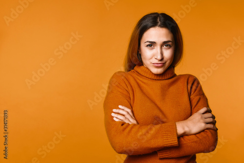 Young girl has cunning look and crossed her hands standing on the orange banner background © IVASHstudio