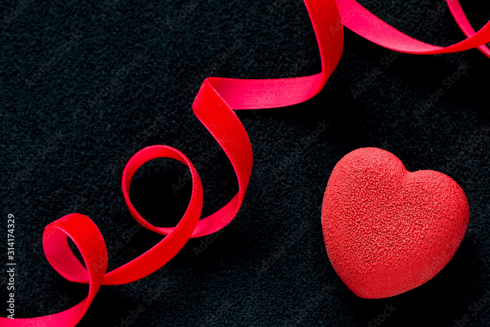 Valentines day concept. Red velvet heart shaped cake on black background with red velvet ribbon