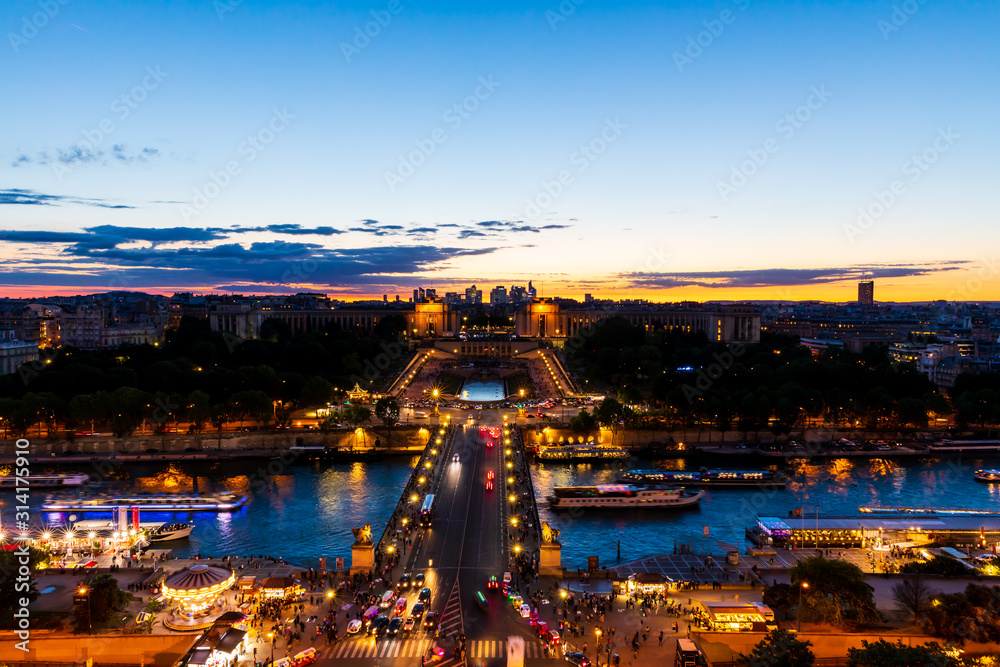 Naklejka premium Panoramic view of Paris at night seen from the first floor of the Eiffel Tower. Long-exposure shot during sunset showing Pont d'Iéna (Jena Bridge), a bridge spanning the River Seine.