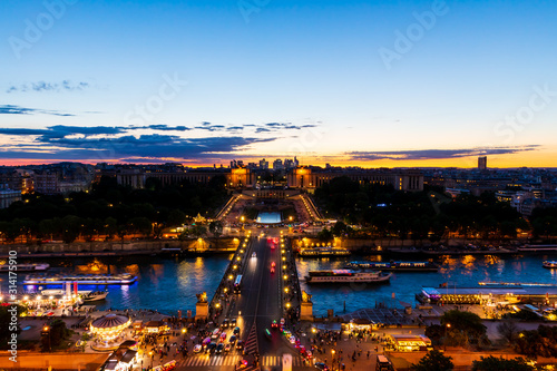Panoramic view of Paris at night seen from the first floor of the Eiffel Tower. Long-exposure shot during sunset showing Pont d'Iéna (Jena Bridge), a bridge spanning the River Seine.