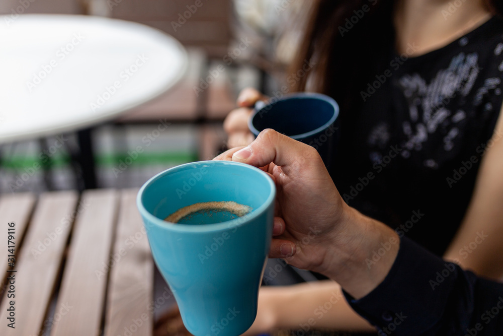 Close-up of mugs in the hands of a young couple drinking coffee. Image of two cups of coffee held by the hands of two lovers Close-up of mugs in the hands of a young couple drinking coffee. Image of two cups of coffee held by the hands of two lovers