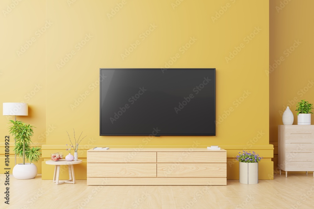 Fototapeta premium Makieta Smart TV w nowoczesnym salonie z lampą, stołem, kwiatem i rośliną na żółtym tle ściany.