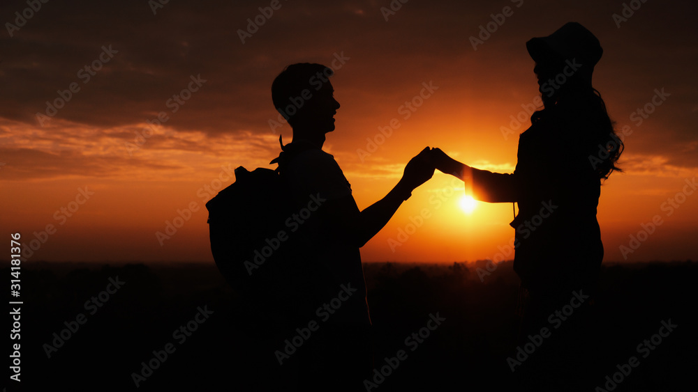 silhouette of lover couple having romantic moment holding hand in hand with background og sunset