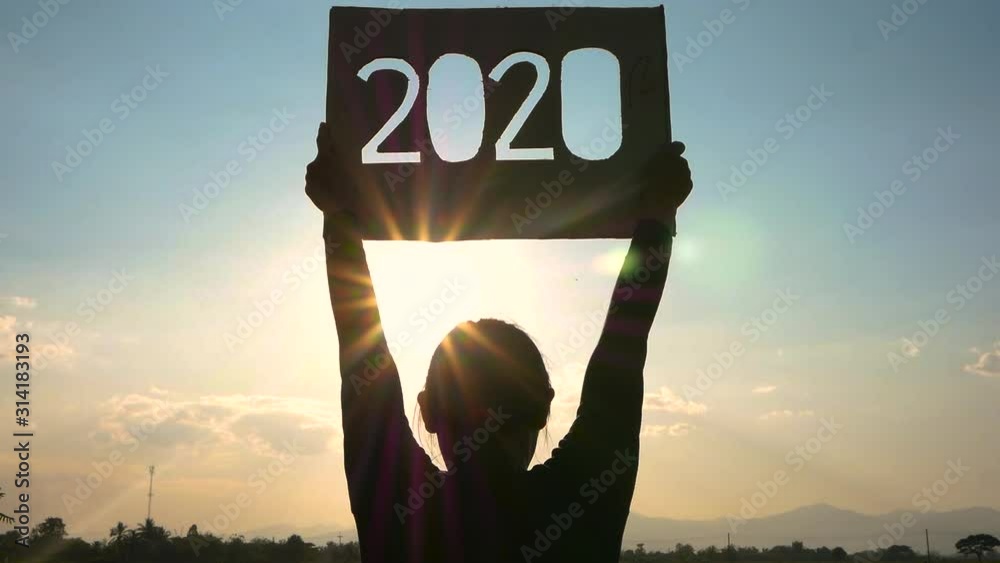 Silhouette of woman holding recycle cardboard with 2020 text over sunset sky background and the sunshining through the text. Concepts of New Year and celebration.