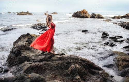 Woman in red dress stands on a cliff with a beautiful sea view and dramatic clouds