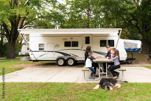 Young family playing cards at campsite in front of camper