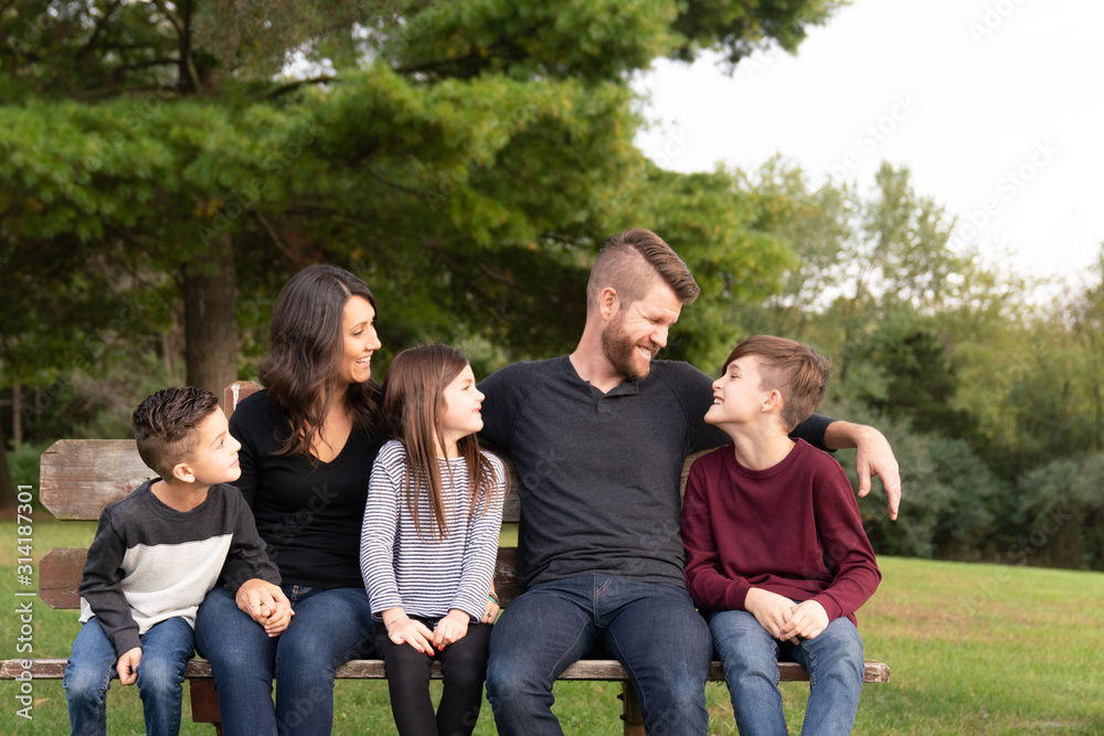 Family sitting on park bench laughing together Family sitting on park bench laughing together
