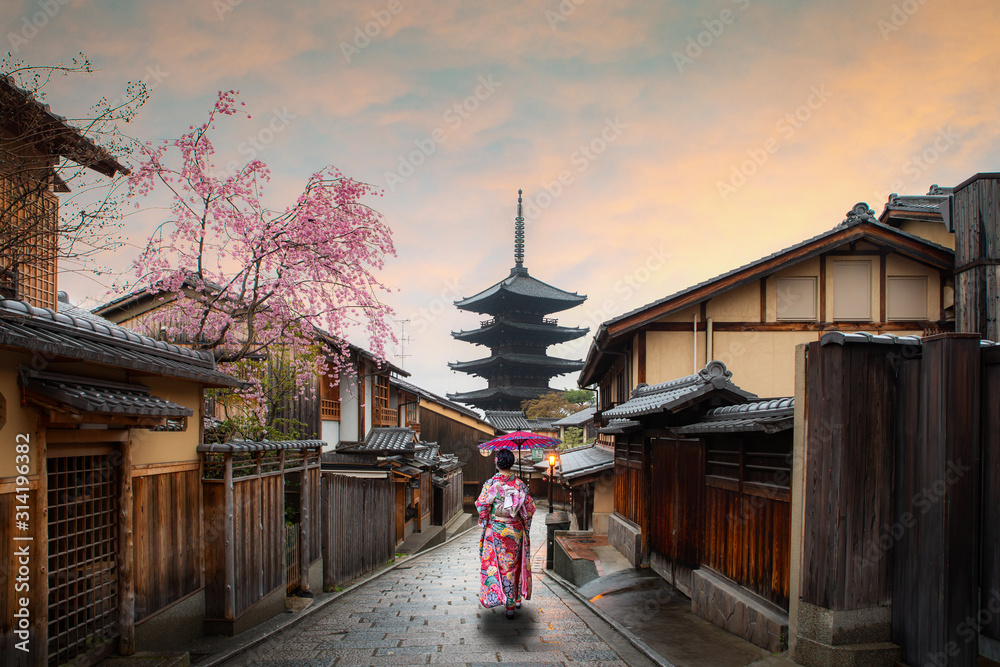 Naklejka premium kobieta podróżująca ubrana w tradycyjne japońskie kimono z czerwonym parasolem zwiedzanie słynnej ulicy Sannen Zaka z historycznym budynkiem domu z kwiatem wiśni wiosną, Kioto, Japonia.