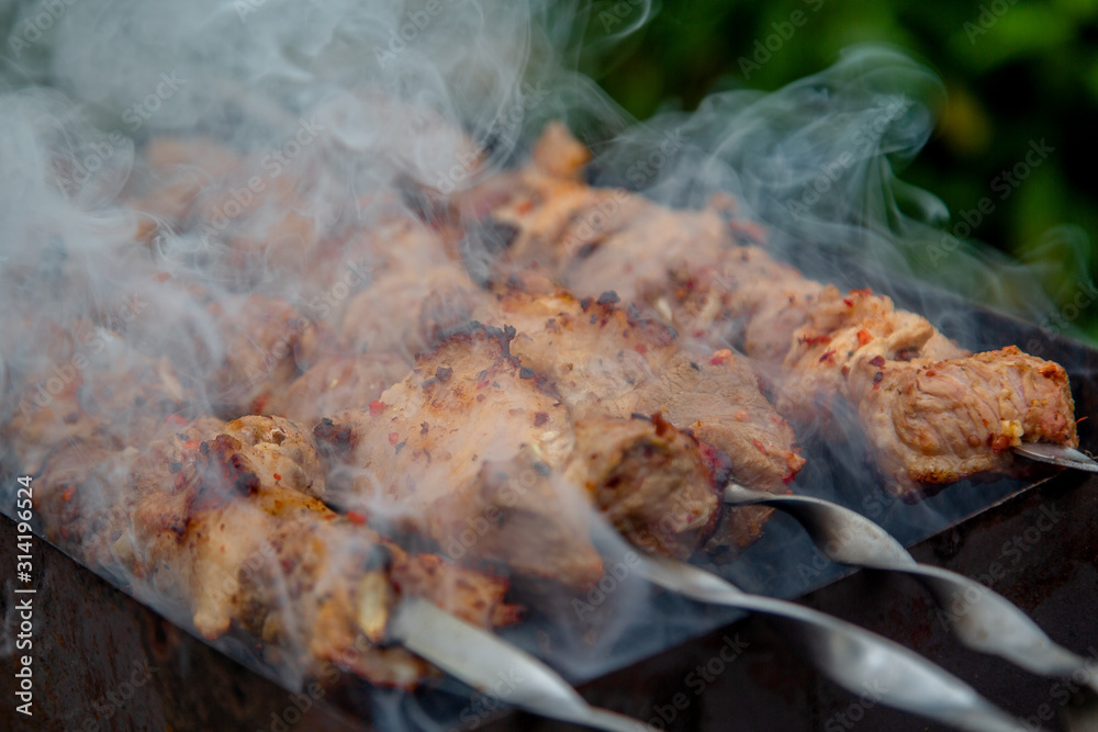 Meat on a skewer cooked on coals. Caucasian cuisine. Charming smoke BBQ outdoor. Meat on a skewer cooked on coals. Caucasian cuisine. Charming smoke BBQ outdoor.