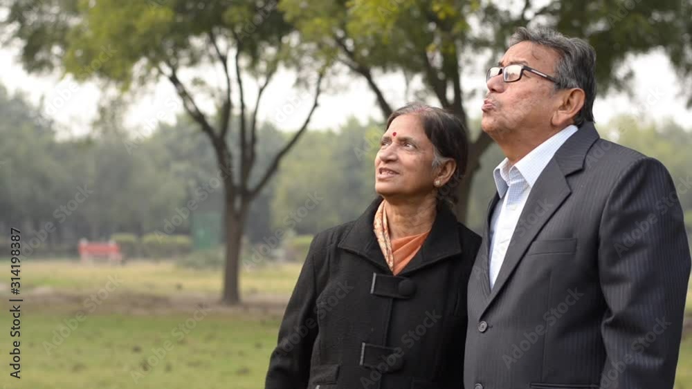 Lifestyle portrait shot of a happy looking senior retired Indian couple in park/outdoor. The wife looks and talks to her husband pointing at something in the distance during winters in New Delhi,India Lifestyle portrait shot of a happy looking senior retired Indian couple in park/outdoor. The wife looks and talks to her husband pointing at something in the distance during winters in New Delhi,India