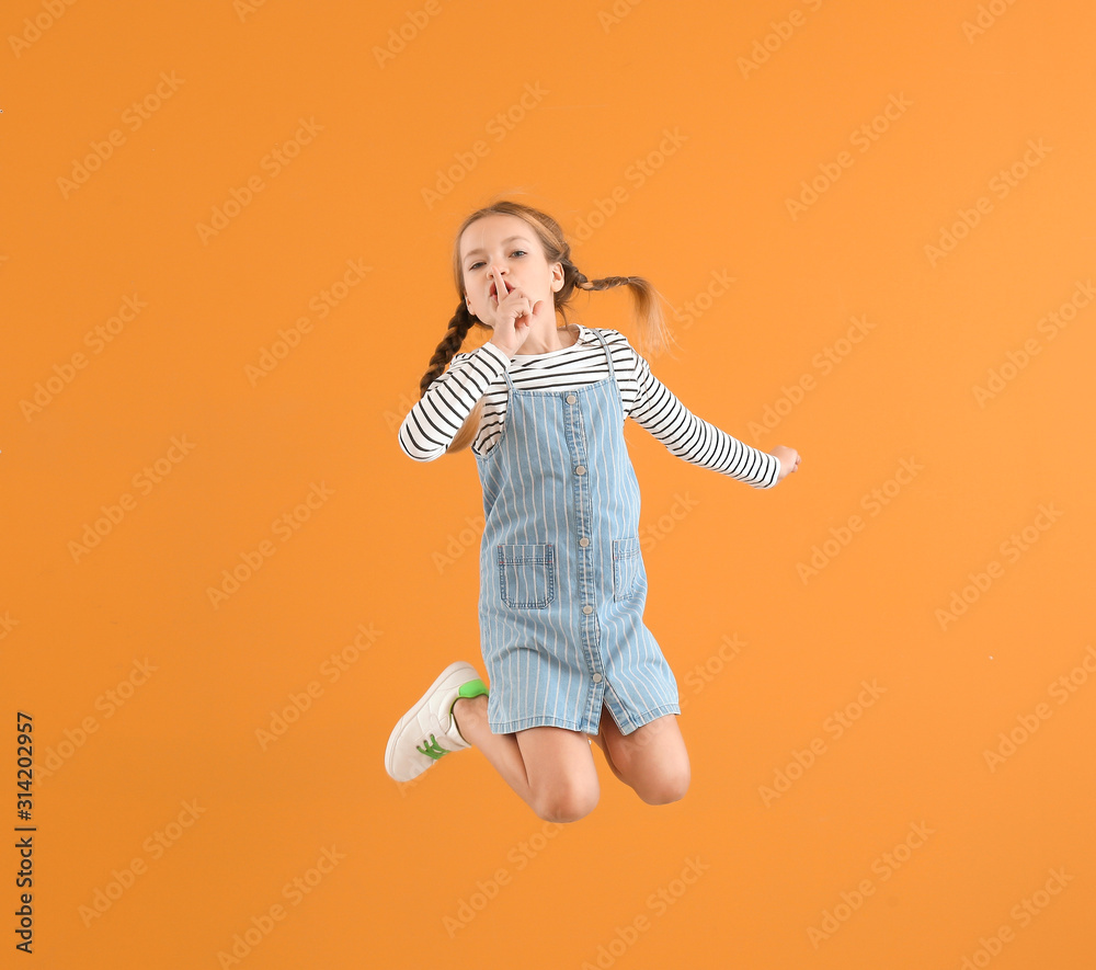 Jumping little girl showing silence gesture on color background Jumping little girl showing silence gesture on color background