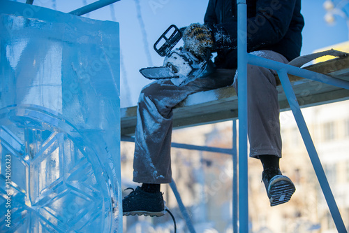 The sculptor cuts ice contours from ice with a chainsaw for Christmas
