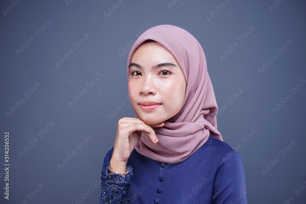 Headshot of a beautiful Muslim female model in a modern kebaya with maroon hijab, an Asian Muslim traditional dress isolated on grey background. Eidul fitri fashion and lifestyle portrait concept. Headshot of a beautiful Muslim female model in a modern kebaya with maroon hijab, an Asian Muslim traditional dress isolated on grey background. Eidul fitri fashion and lifestyle portrait concept.