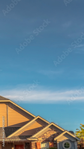 Vertical frame House exterior with view of the gable roof with gable windows against blue sky