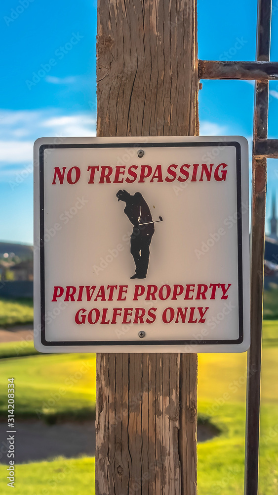 Vertical frame No Trespassing sign with blurry golf course homes mounntain and sky background