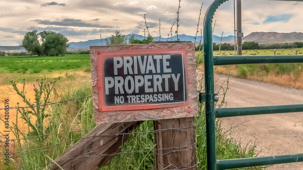 Panorama No Trespassing sign on the wire fence and green metal gate of private property