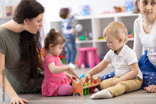 Children playing in kindergarten or daycare centre under the supervision of moms