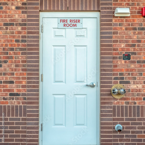 Square Fire Riser Room sign on the white wood door of a building with red brick wall photo