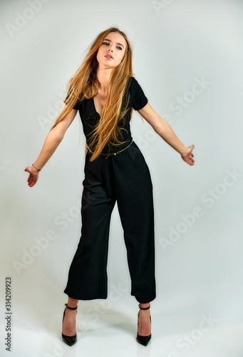 The concept of fashion and style. The model stands in different poses in front of the camera. Full-length portrait of a pretty blonde girl with long hair and excellent make-up on a white background.