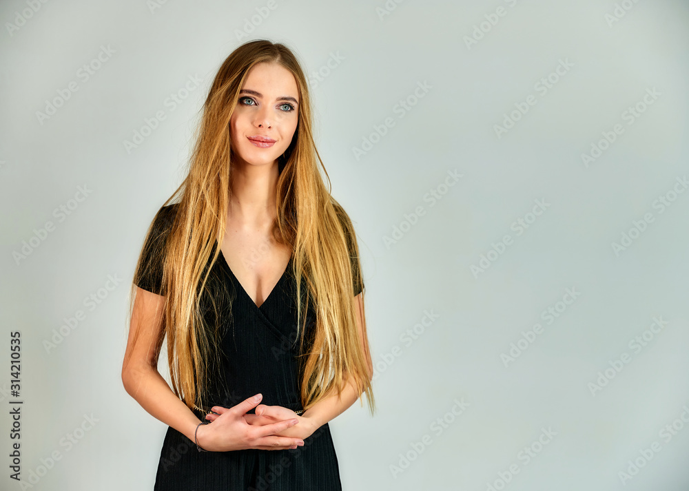 Fototapeta premium The concept of fashion and style. Portrait of a pretty blonde girl with long hair and great makeup on a white background. The model stands in different poses in front of the camera.