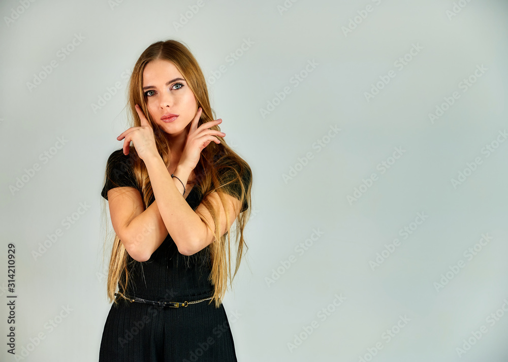 Fototapeta premium The model stands in different poses in front of the camera. The concept of fashion and style. Portrait of a pretty blonde girl with long hair and great makeup on a white background.