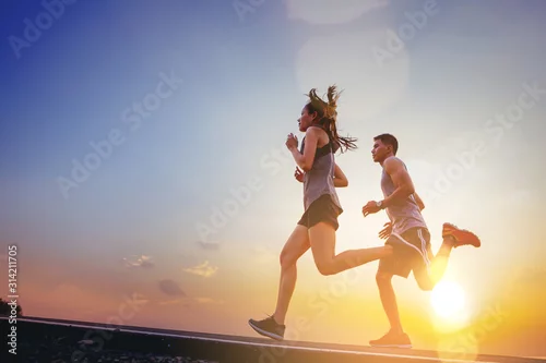 Fototapeta Young couples running sprinting on road. Fit runner fitness runner during outdoor workout with sunset background