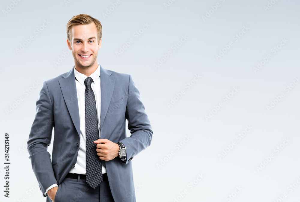 Portrait of happy smiling young businessman in confident suit, on grey background. Business success concept. - obrazy, fototapety, plakaty 