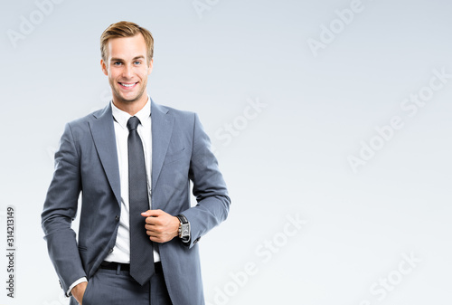 Portrait of happy smiling young businessman in confident suit, on grey background. Business success concept. photo