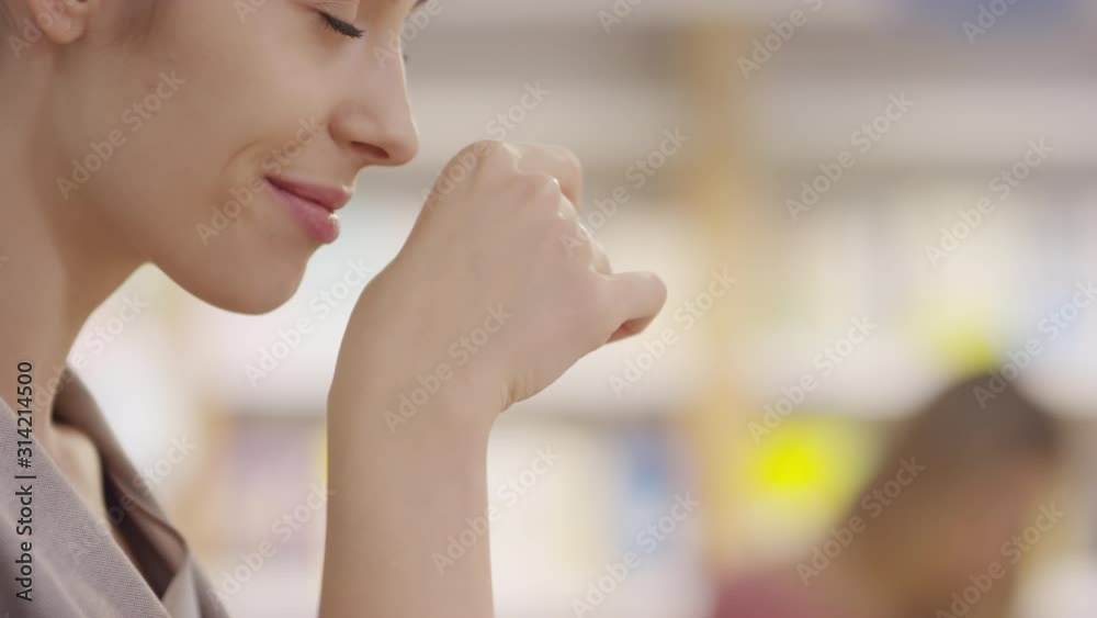 Tilt up shot with close up of attractive young woman smiling and smelling her hand after putting on cream at cosmetic store