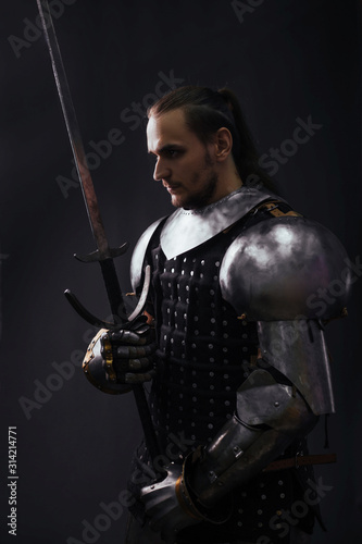 Portrait of a medieval knight with a two-handed sword in the dark. Silhouette Warrior in the studio on a dark background.