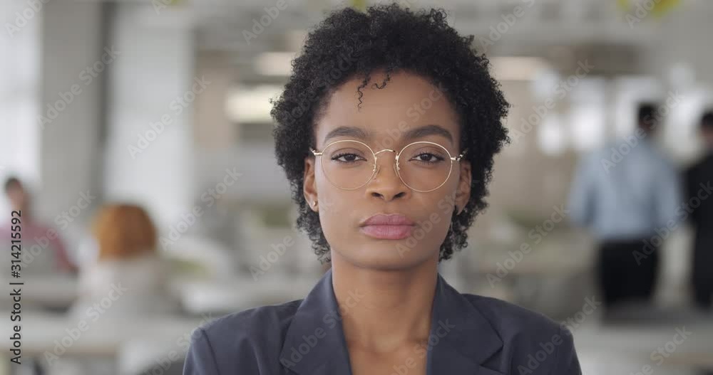 Close up of confident mixed race lady boss looking to camera. Attractive young woman in glasses in modern office workspace. People portraits. Blurred background. Concept of career.