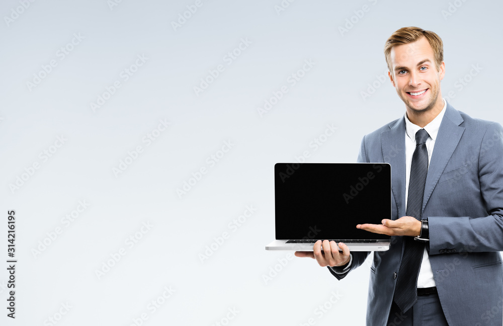 Happy smiling businessman in grey confident suit, showing blank laptop monitor, with copy space for some slogan or text. Success in business concept picture. Happy smiling businessman in grey confident suit, showing blank laptop monitor, with copy space for some slogan or text. Success in business concept picture.