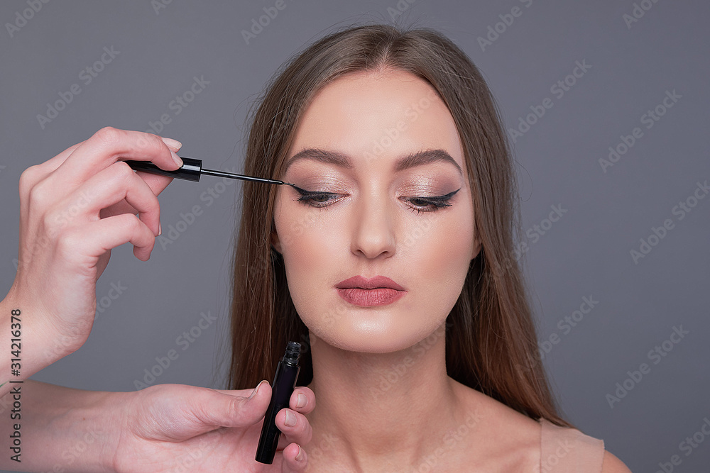 Make-up artist brush black eyeliner on the face of the woman. Young beautiful woman applying make-up by make-up artist