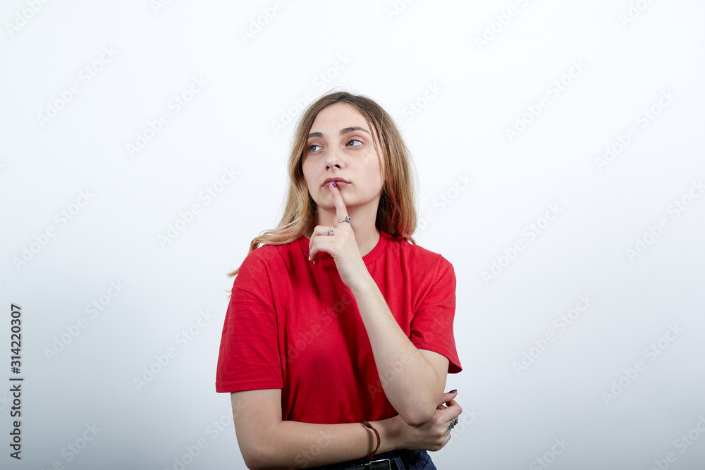 Serious caucasian woman in fashion red shirt keeping finger on mouth, holding hands on stomach, thinking isolated on white background in studio. People sincere emotions, lifestyle concept. Serious caucasian woman in fashion red shirt keeping finger on mouth, holding hands on stomach, thinking isolated on white background in studio. People sincere emotions, lifestyle concept.