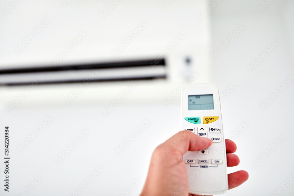 Modern air conditioner unit with a hand holding a remote.