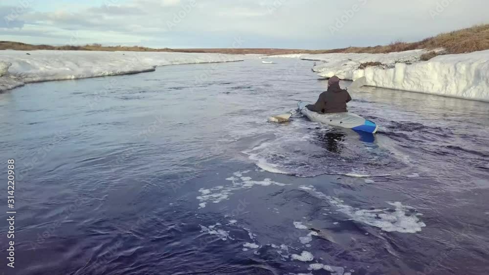 professional canoeist sails in canoe along raging spring river with paddle between banks covered with frozen snow backside professional canoeist sails in canoe along raging spring river with paddle between banks covered with frozen snow backside