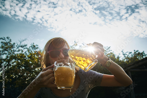 Cute girl playing with two glasses of beer outdoors.